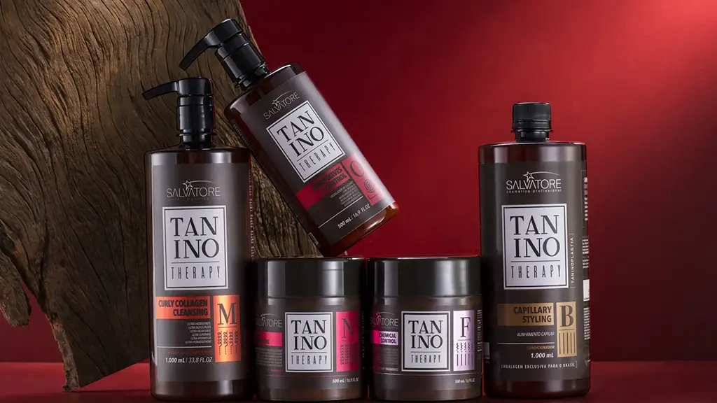 kit Cachos Therapy composto pelos produtos : Produto M - Curly Collagen Cleansing; Produto N - Curly Hidrolipidic; Produto O - Curly Waves Control; Produto B - Capillary Styling Produto F - Chemical Control apoiados em uma base de madeira vermelha e com um fundo liso vermelho escuro com passagem de luz. Atrás dos produto há uma madeira rústica na posição diagonal posicionado no lado esquerdo da imagem.